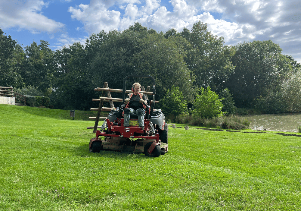 Salariée en insertion des espaces verts qui tond la pelouse avec un tracteur tondeuse